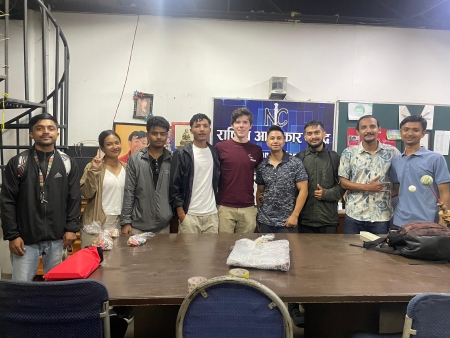 Josiah Shimandle standing in front of a table with eight colleagues from NIC, Nepal