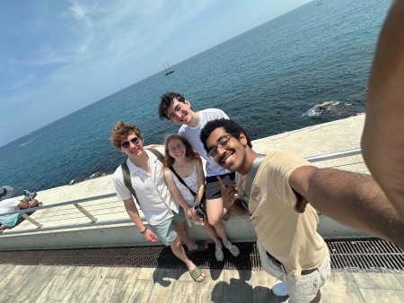 Caleb taking a wide-angled selfie with three others in front of a railing that overlooks the sea