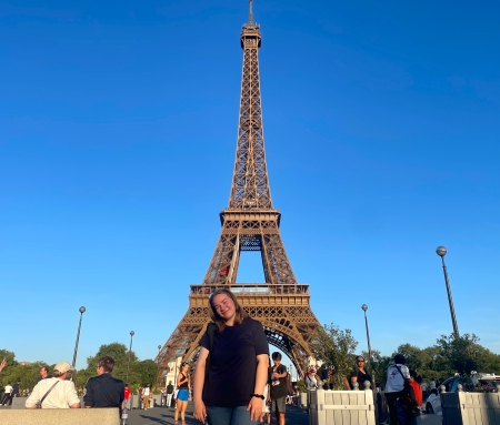 Emilia smiling in front of the Eiffel Tower on a sunny cloudless day