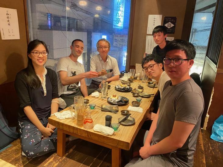 Demi Fang and five other lab mates seating on a traditional Japanese dining table at a restaurant in Tokyo with serving plates, chopsticks and drinks on the table