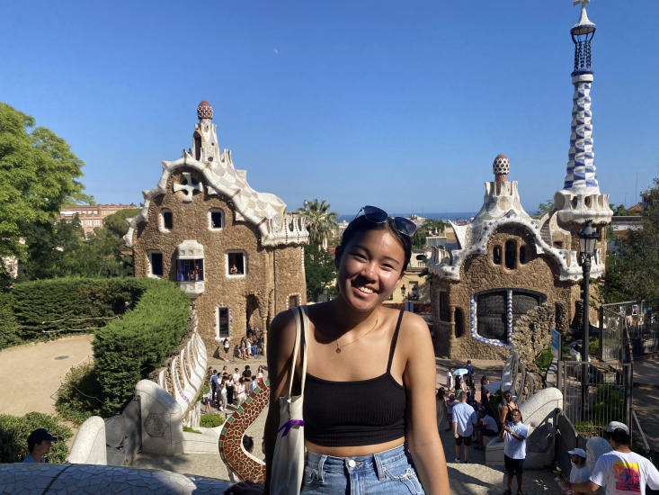 Sally Zhao at Parc Güell with two geometrical buildings at the park entrance in the background