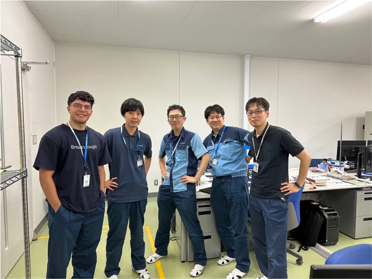 Michael Iglesias with his hands in his pockets standing far left with four colleagues in a white-walled office with grey desks and office chairs at ULVAC Japan 