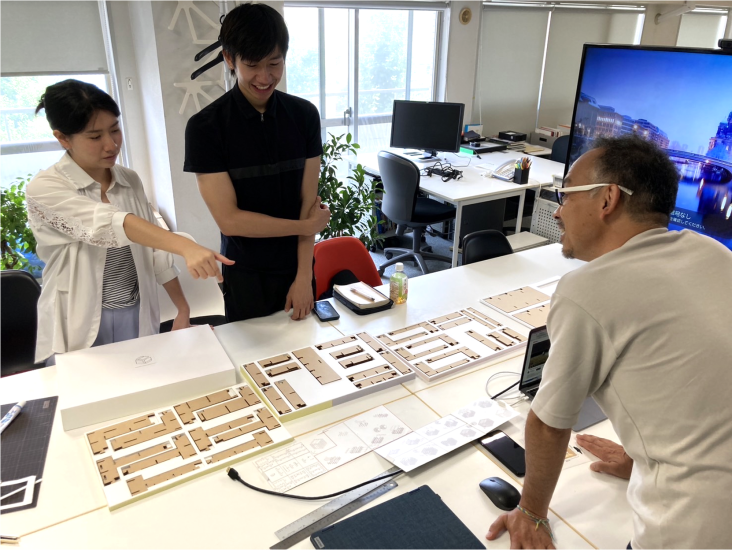 Michael Tan standing over a table with printed papers of brown blocks, discussing work with colleagues at KMDW