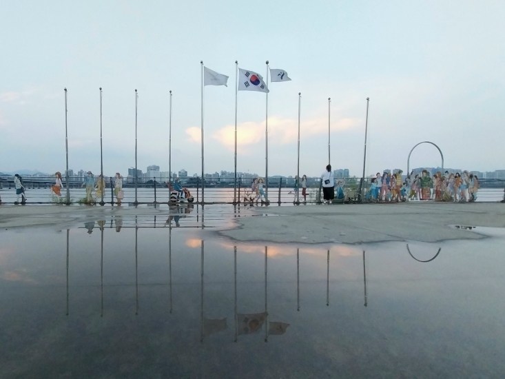 Cloudy day with three flags (South Korea flag in the middle) hung high on a pole 