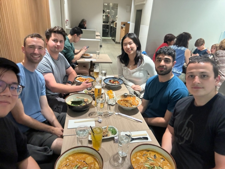 A selfie with five colleagues and Jocelyn Zhi sitting at the end of the table eating a meal