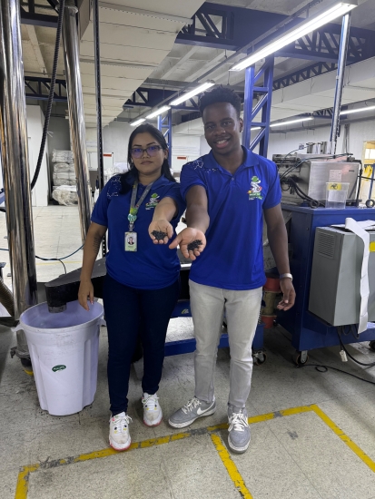 Andre Hamelberg and colleague holding out one hand with some black beads in their hand in a factory