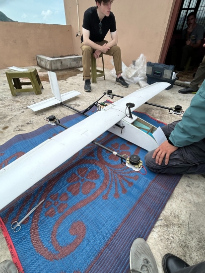 Josiah Shimandle sitting on a plastic stool looking at the white drone wing on a mat on the ground