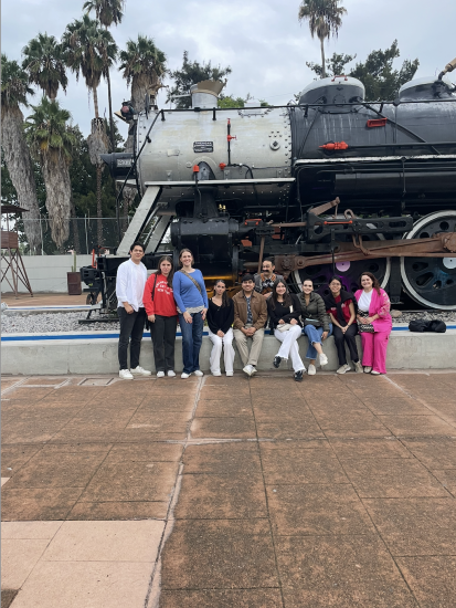 Amanda Chung with 9 others in front of a train with palm trees behind it