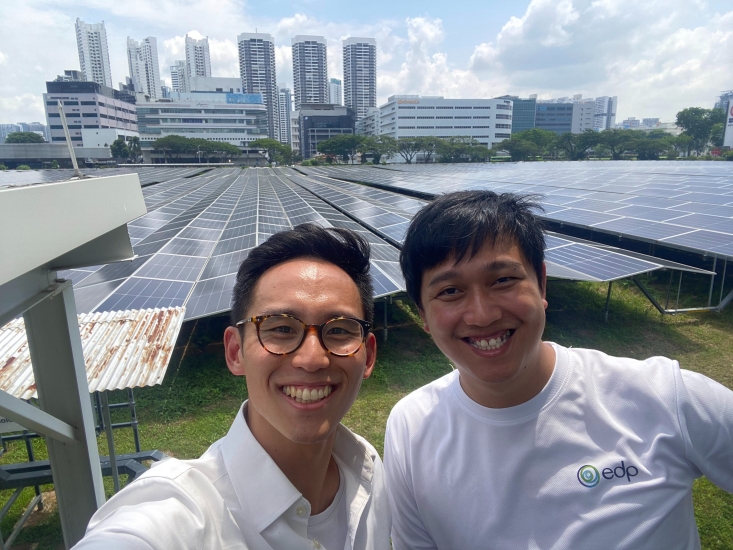 Kevin Yi taking a selfie with someone with rows of solar panels and the Singapore skyline in the horizon