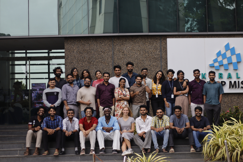 Sophia Woodbury seated on the steps in front of Kerala Startup Mission in India with 27 other colleagues