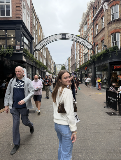 Harley Carroll in a white sweater in the middle of a busy pedestrian street on Carnaby Street