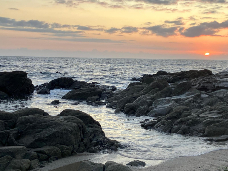 Picture of the waves crashing into rocks at the beach during a sunset 