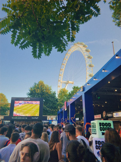 A picture of the London Eye in a distance with a crowd in front of a screening of the World Cup