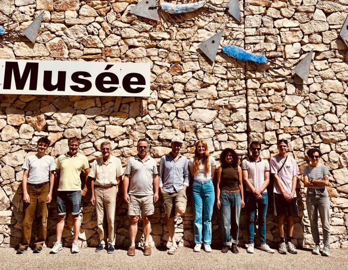 Catherine H. and nine others standing in a row in front of a rock wall with the sign on top Musée