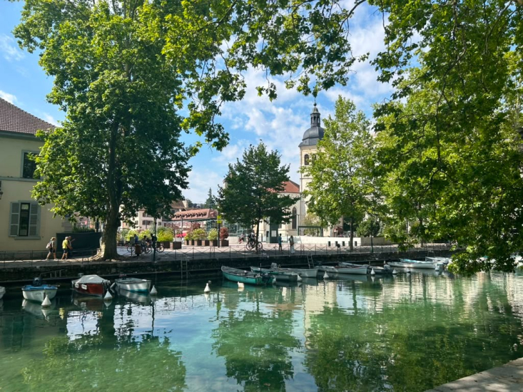 A french canal with green trees along the canal and  buildings in the background